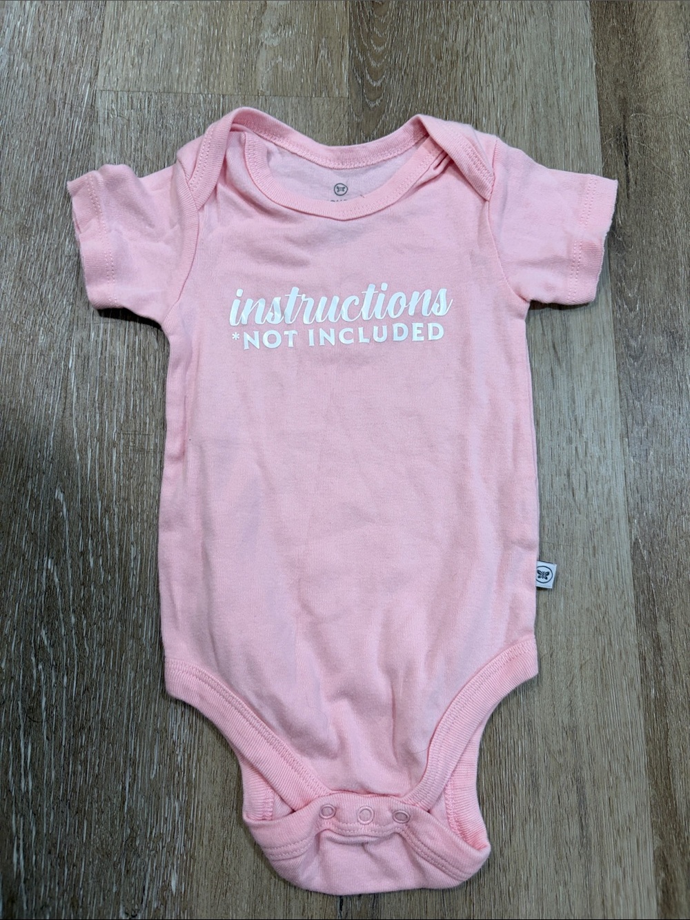 The Honest Company Pink Baby Bodysuit with "instructions not included" Text